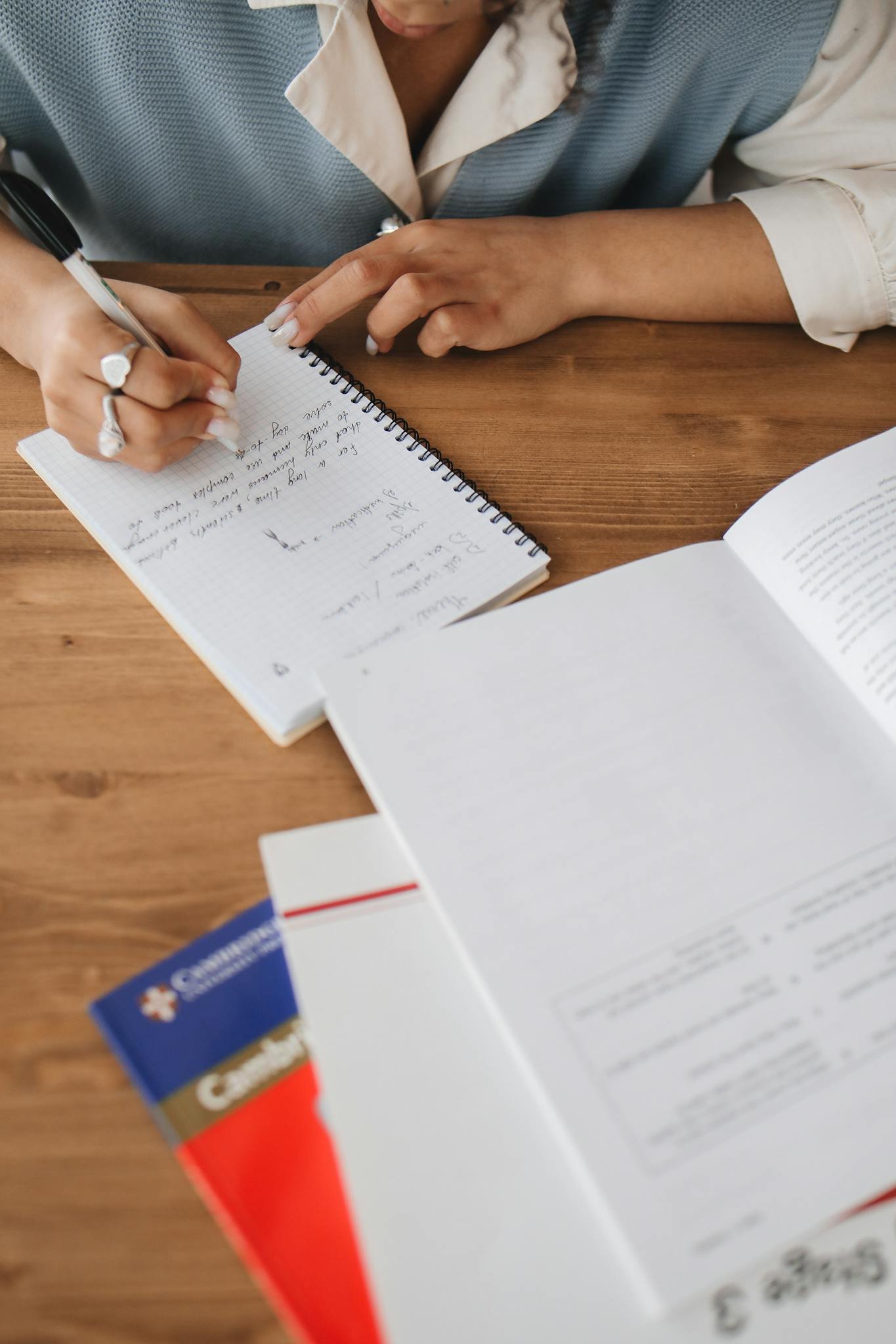 Close-up of a student writing in a notebook, studying at a wooden desk.