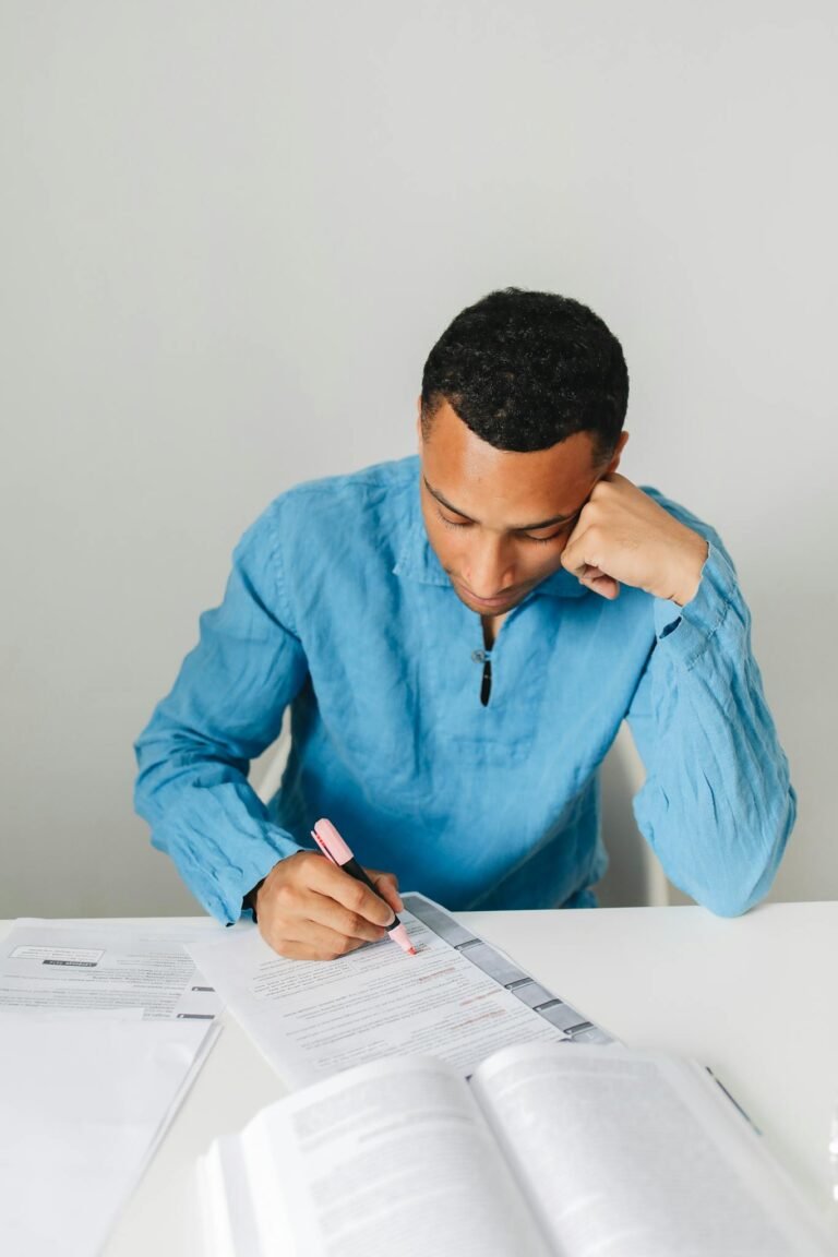 Young man in blue shirt studying with highlighter and book, focused on learning.